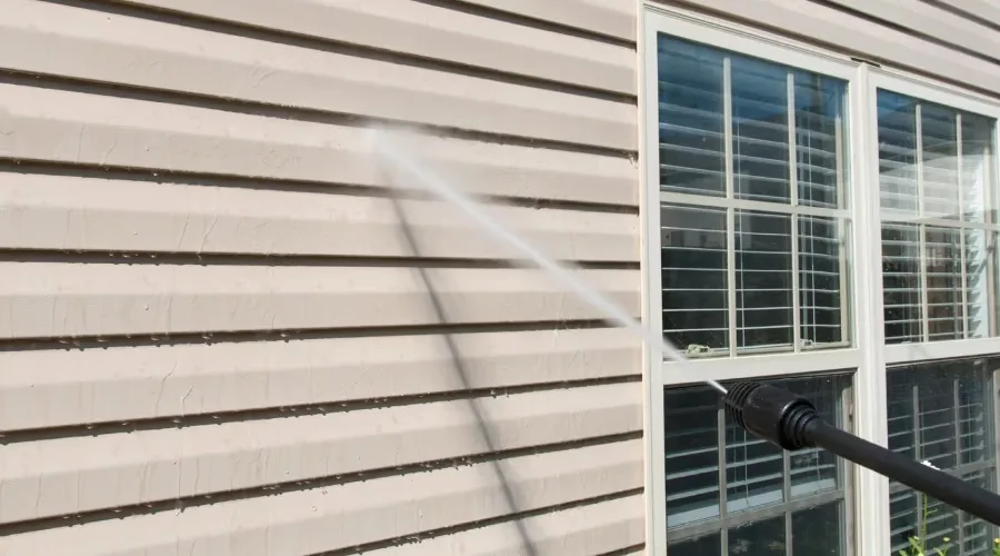 Spray wand soft washing vinyl siding beside a window