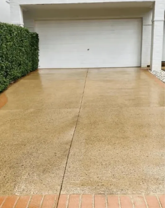 Concrete driveway mid-clean with a clear line between washed and unwashed sections
