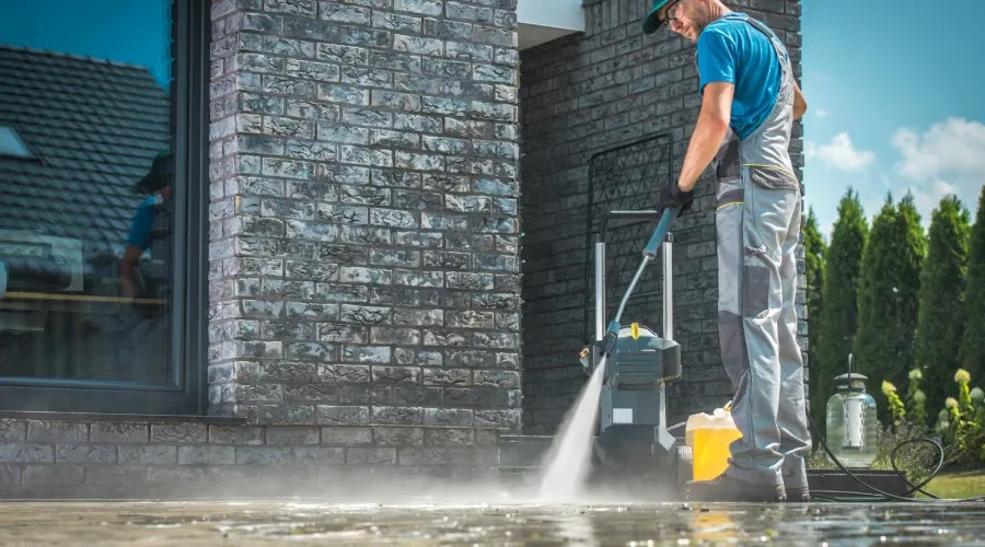 Technician pressure washing a stone patio beside a Wesley Chapel home